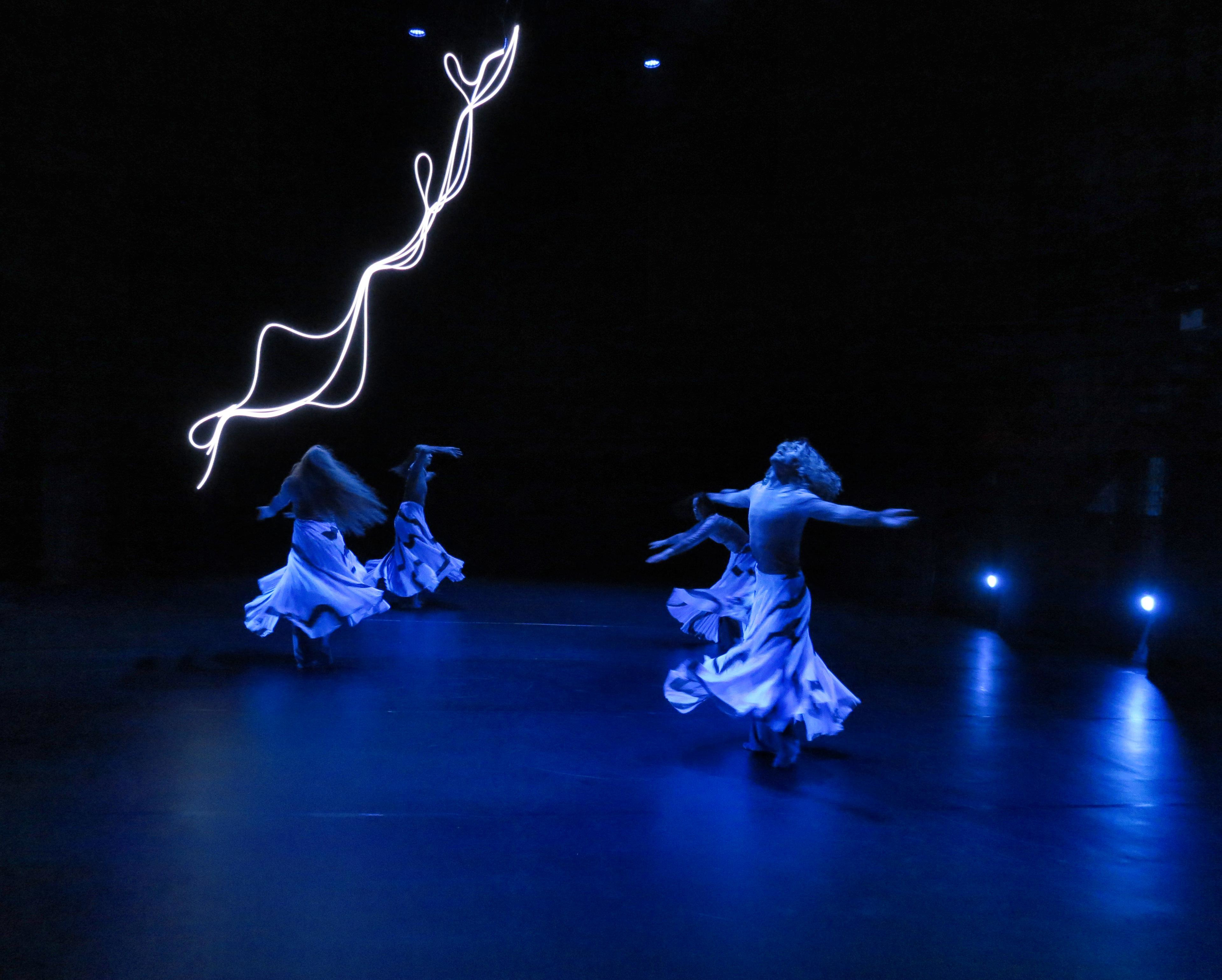 a group of dancers in skirts twirling rapturously against the the bright light sculpture